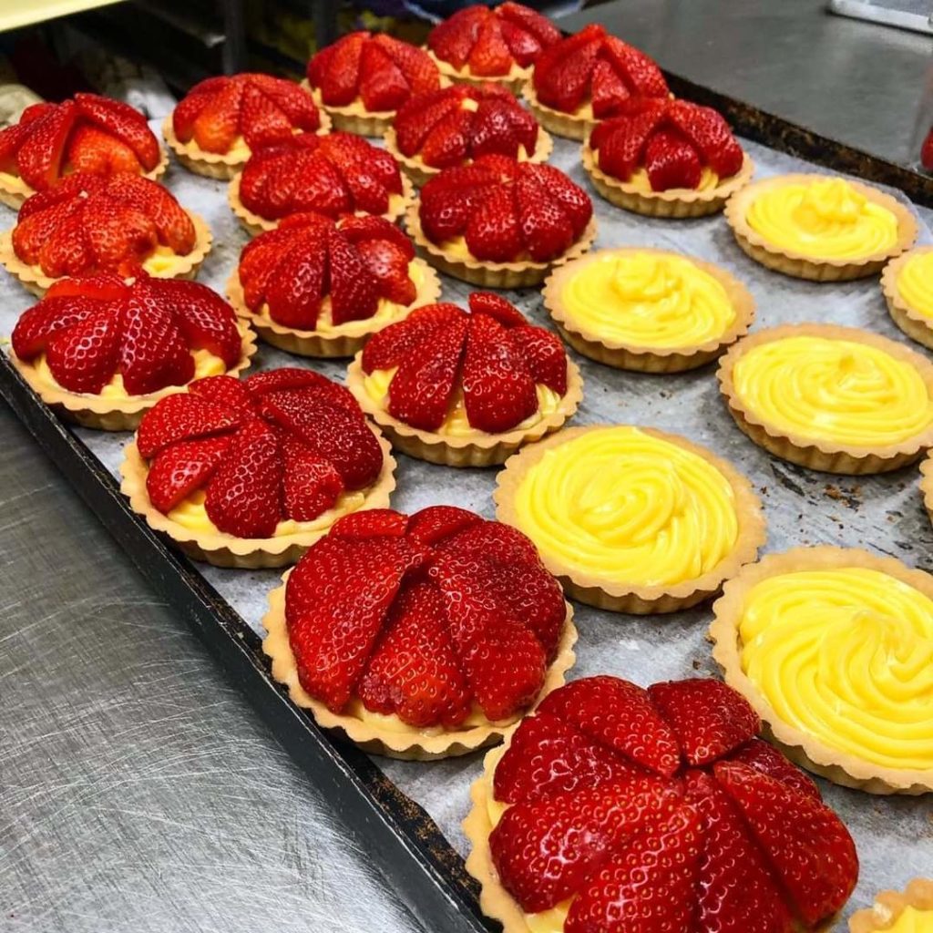 Bright red strawberry tarts and custard tarts on a baking tray