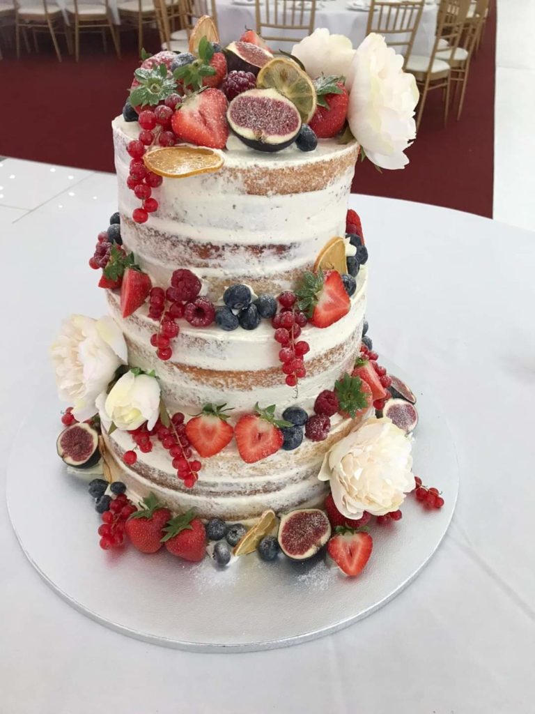 Three tier white cake with colourful fruits and flowers