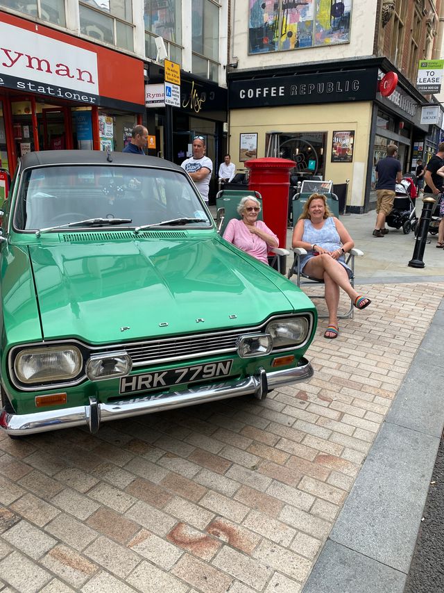 Two ladies sitting on deckchairs next to a green car